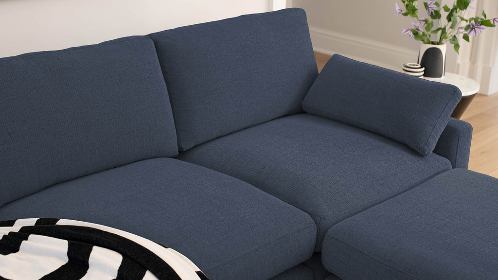 Close-up of a modern navy blue fabric sectional sofa with a matching cushion and a black-and-white striped throw blanket.