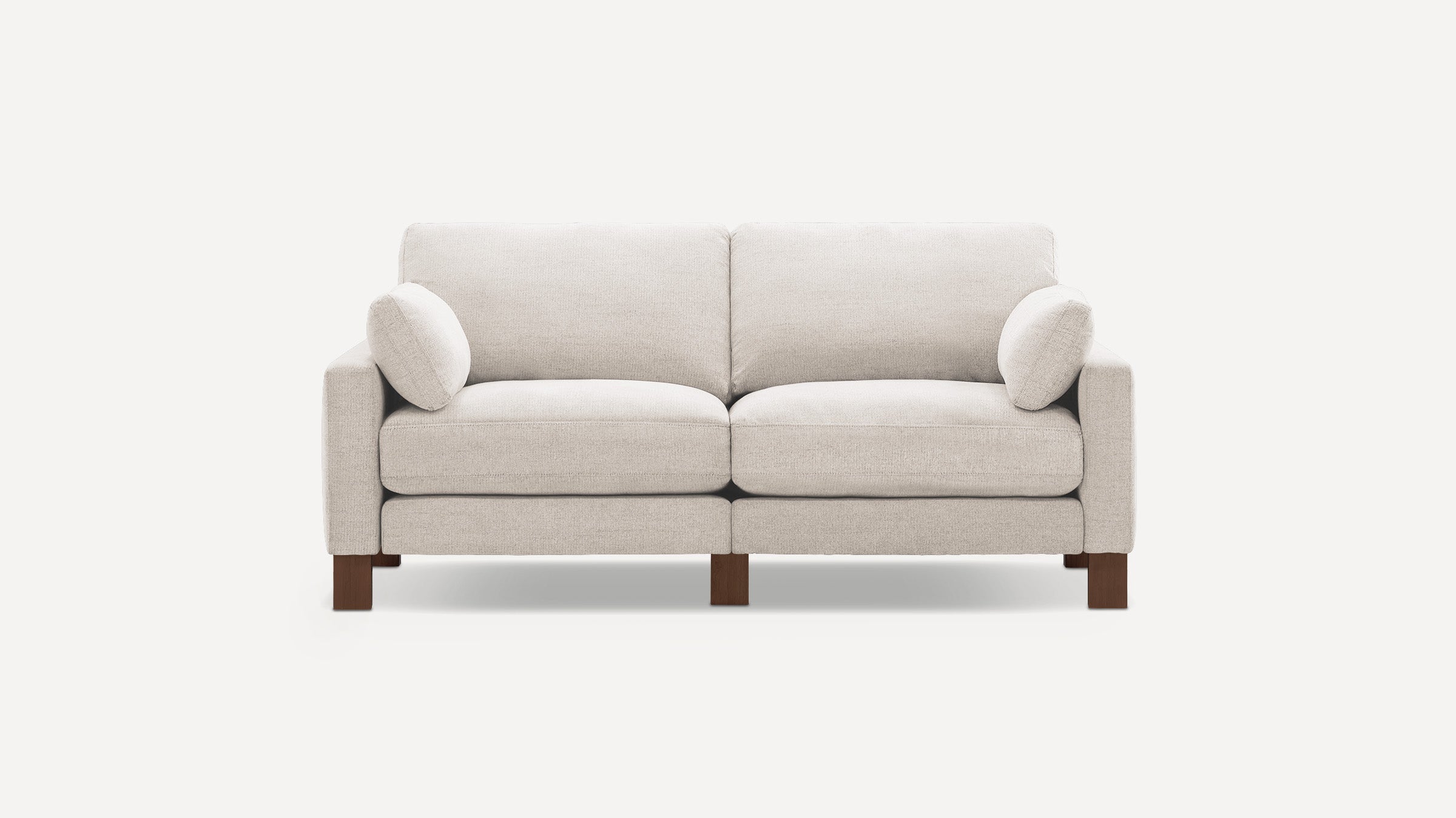 Light beige upholstered two-seater sofa with plush cushions and wooden legs, featuring two small side pillows.