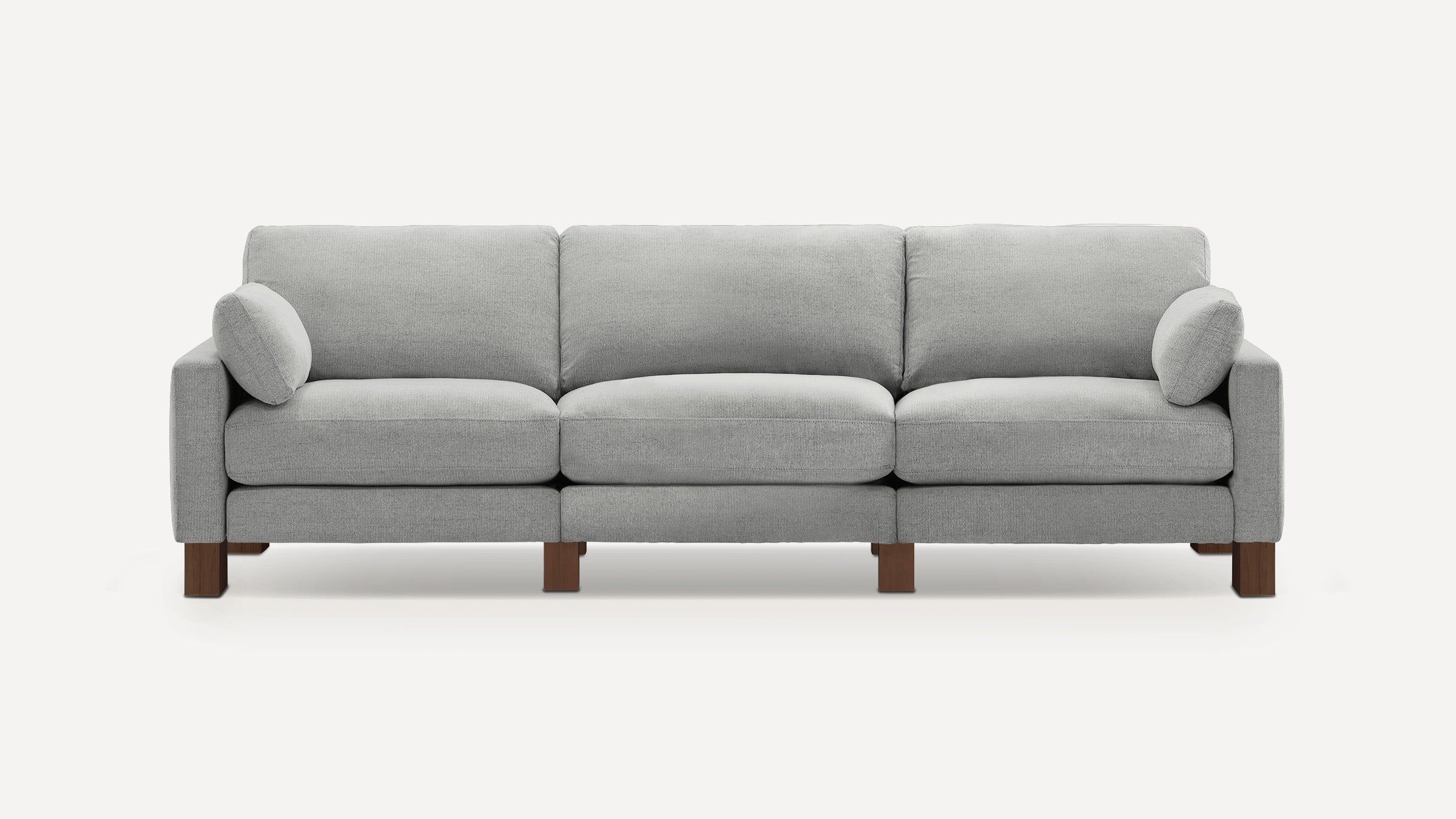 Modern three-seater sofa with light gray fabric upholstery, square armrests, and dark wooden legs, featuring two matching cylindrical pillows.