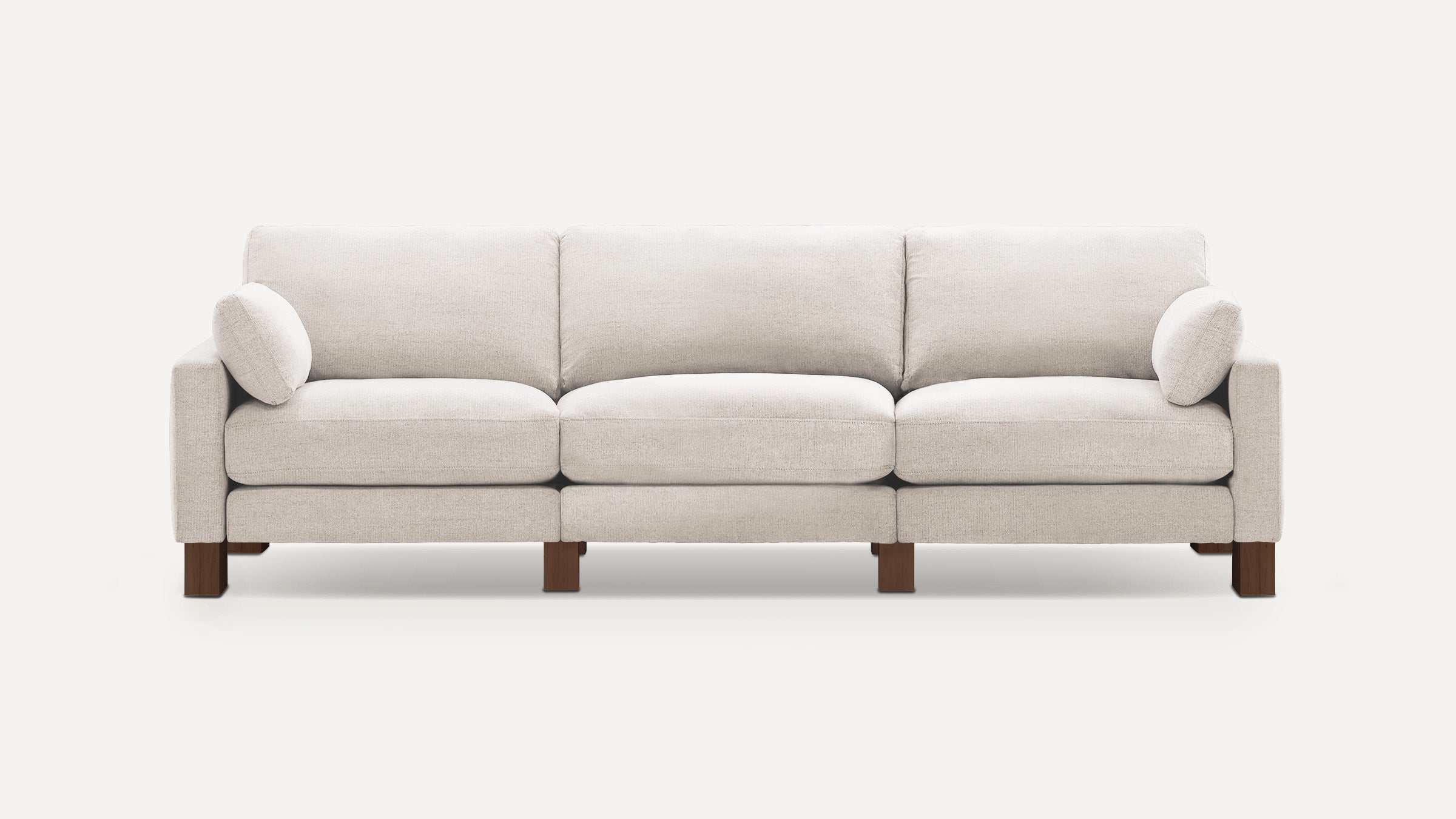 Modern three-seater beige fabric sofa with cushioned seats, backrests, and two round side pillows on wooden legs.