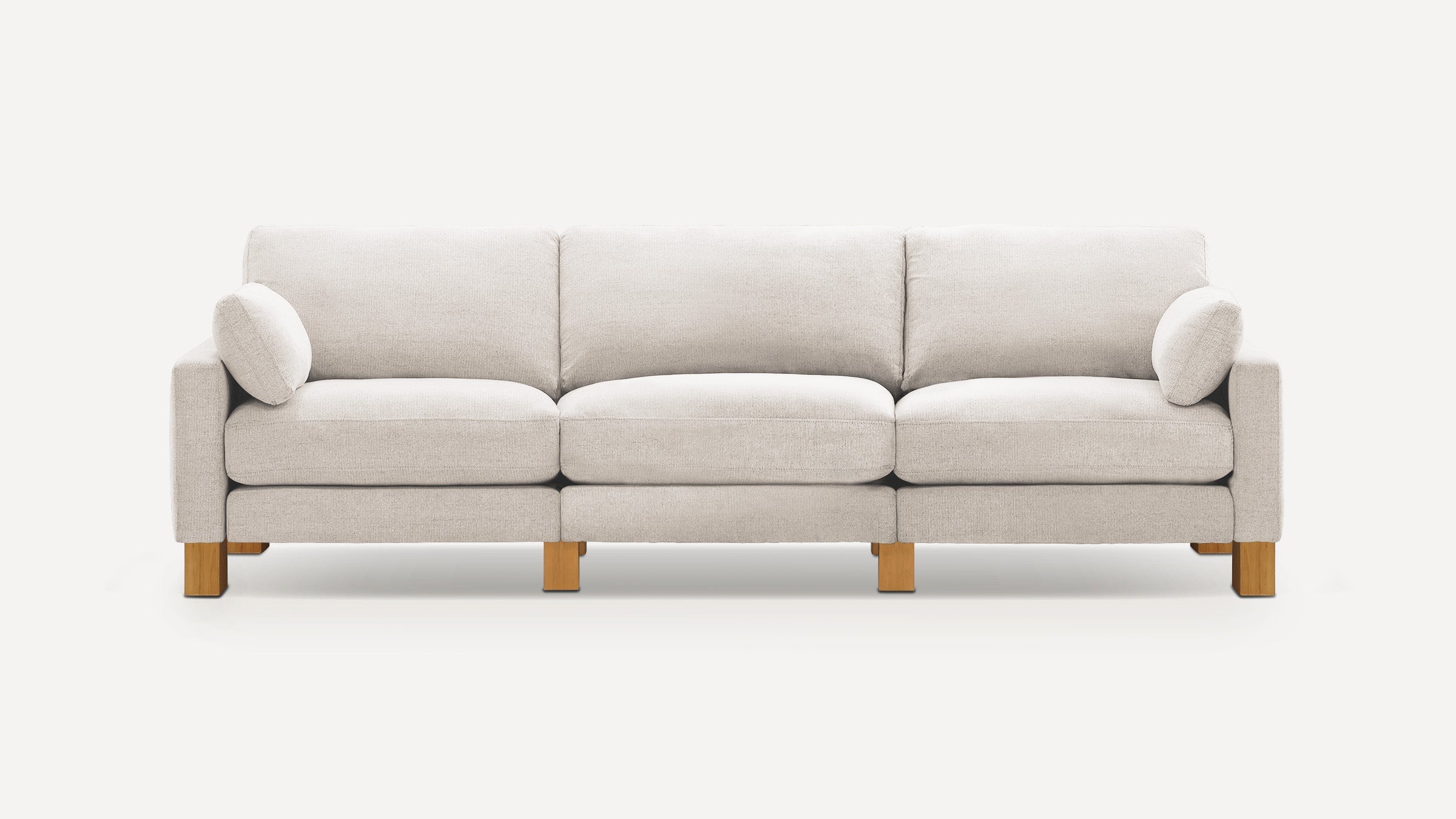 A modern three-seat beige fabric sofa with two matching cylindrical pillows and wooden block legs on a white background.