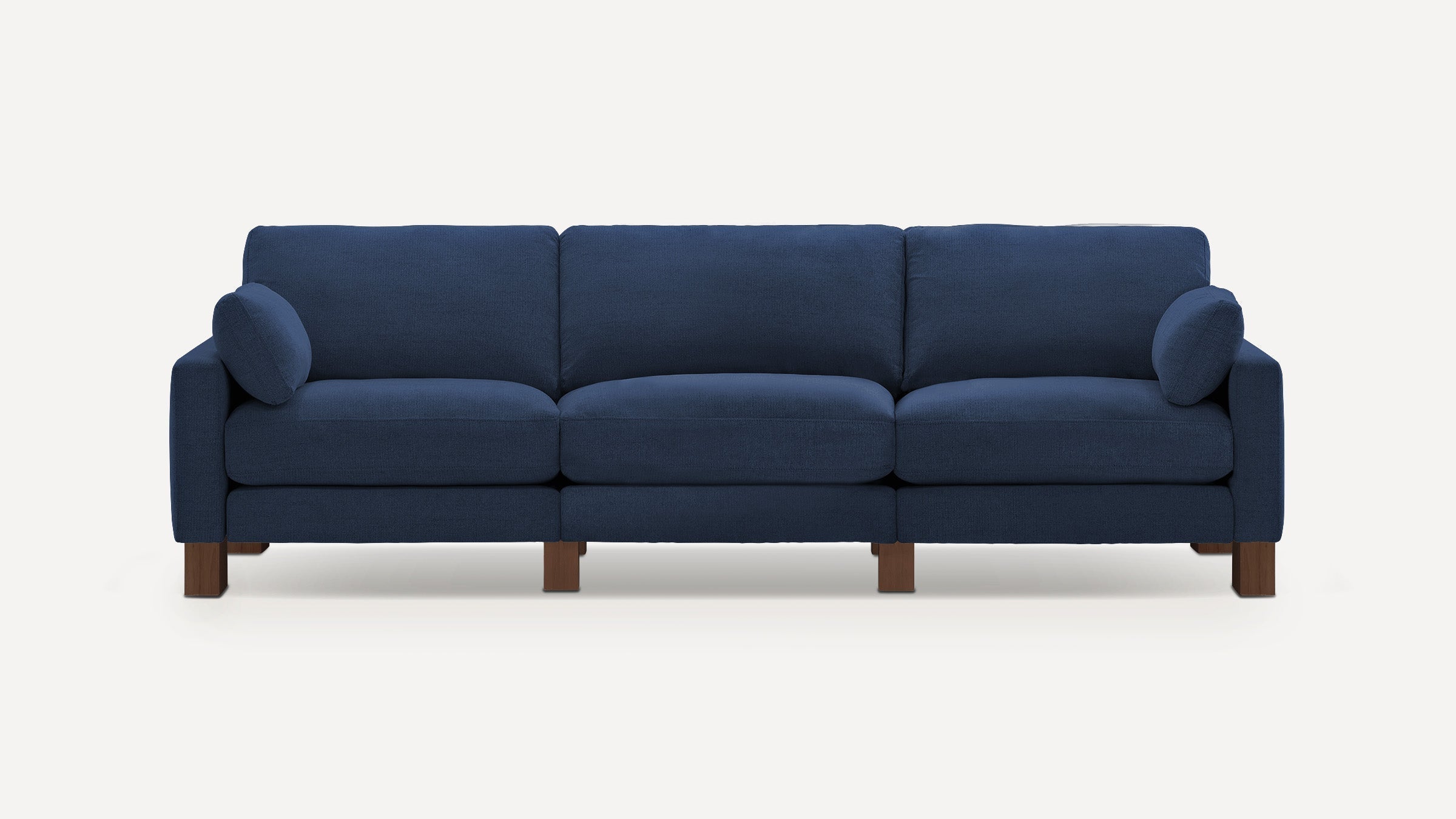 Dark blue three-seater sofa with plush cushions, padded armrests, and wooden block legs against a light background.