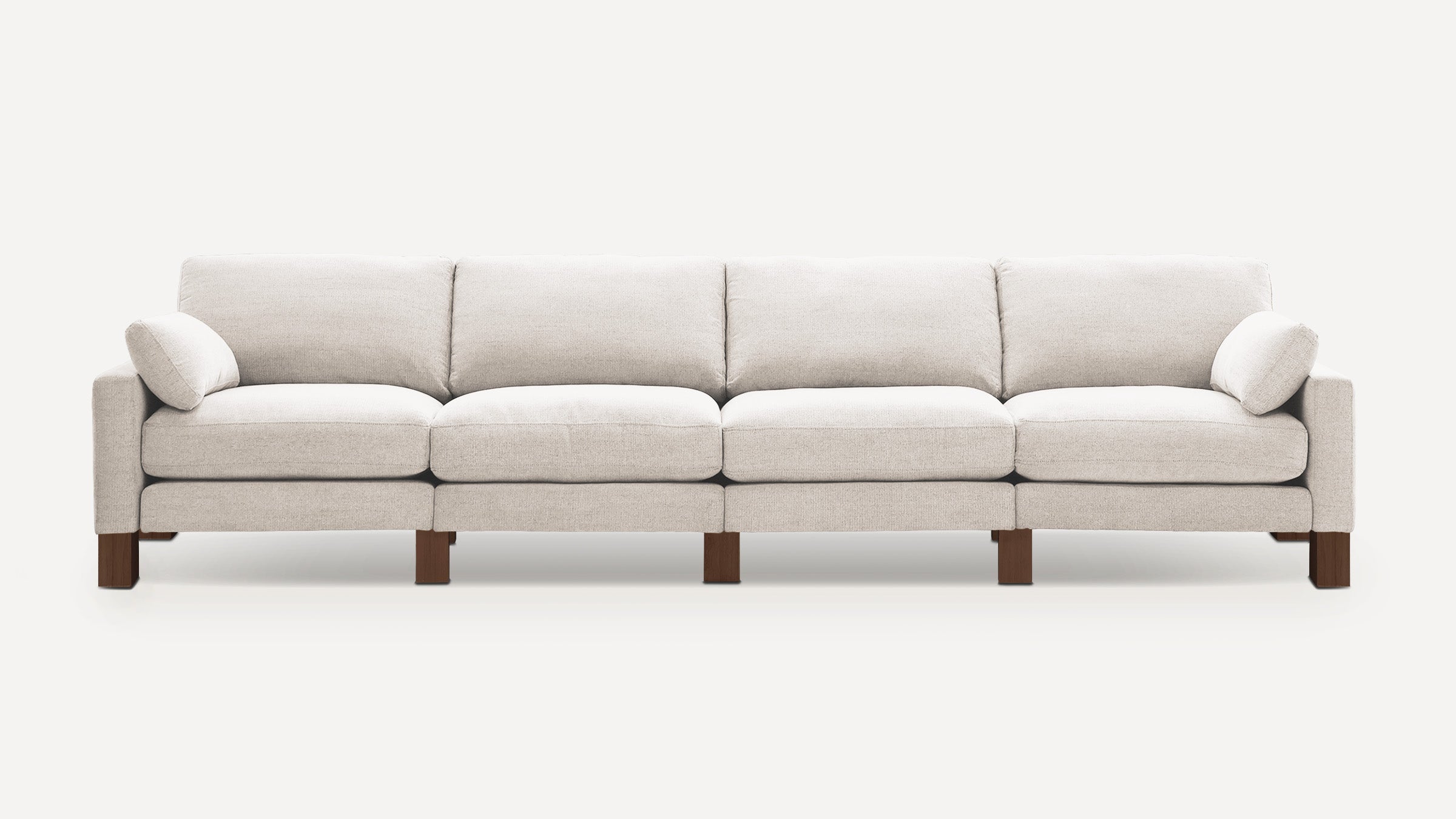 Modern, light beige four-seater sofa with clean lines, plush cushions, wooden legs, and two matching side pillows.