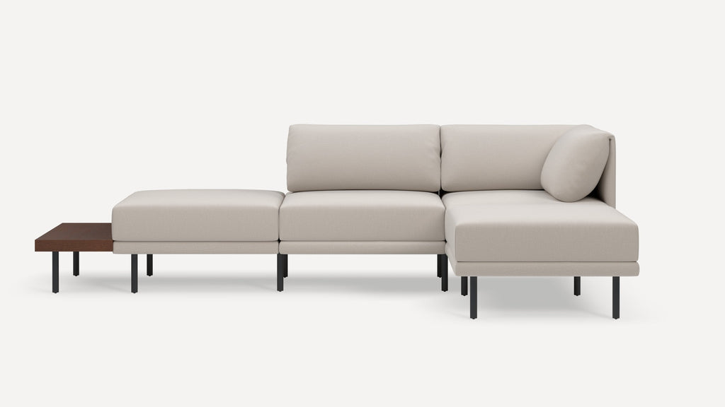 Modern beige sectional sofa with clean lines, supported by black metal legs, and featuring an attached wooden side table on the left.