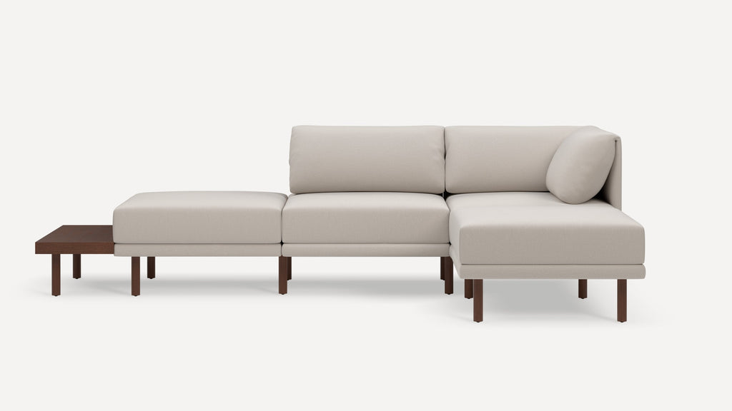Modern beige sectional sofa with wooden legs, chaise lounge, and attached wooden side table on left side.