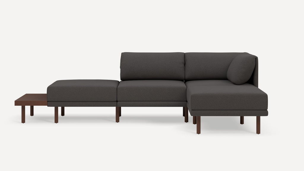 Modern dark gray sectional sofa with wooden legs and an attached low wooden side table on one end.