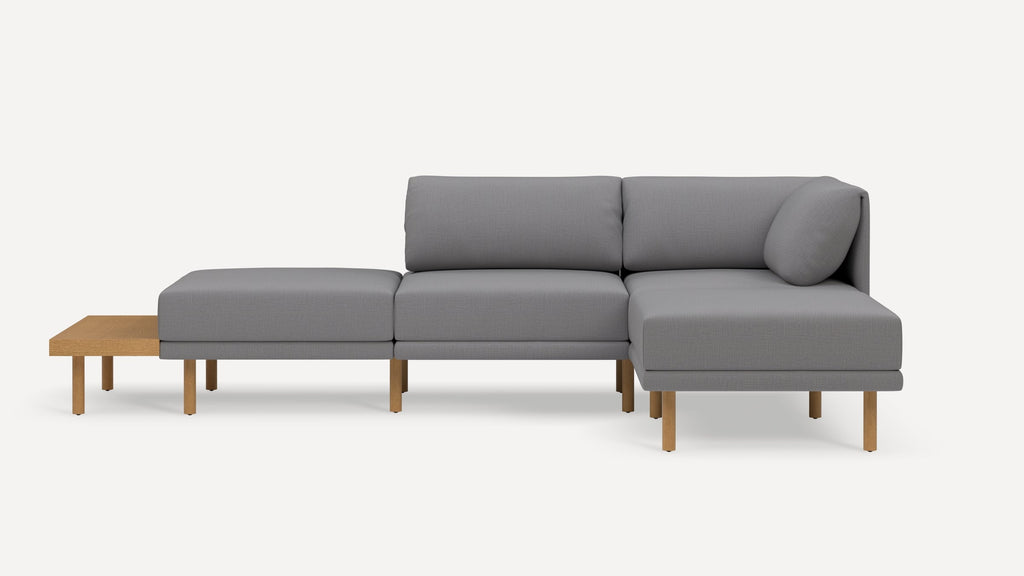 Modern gray sectional sofa with wooden legs and built-in wooden side table, minimalist design on white background.