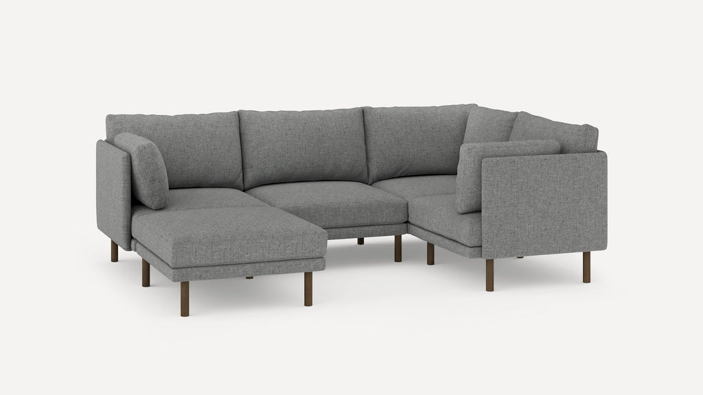 Modern L-shaped sectional sofa in gray fabric with wooden legs, featuring comfortable back cushions and a chaise lounge on the left side.