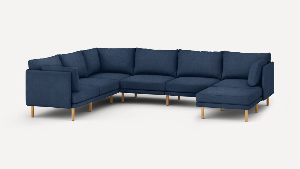 Large modern navy blue fabric sectional sofa with wooden legs, featuring an L-shape and plush back cushions.