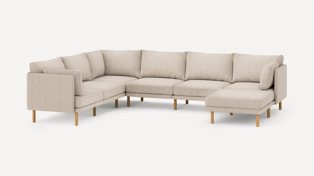 Beige L-shaped sectional sofa with wooden legs, clean modern design, cushioned back, and additional side pillows for comfort.