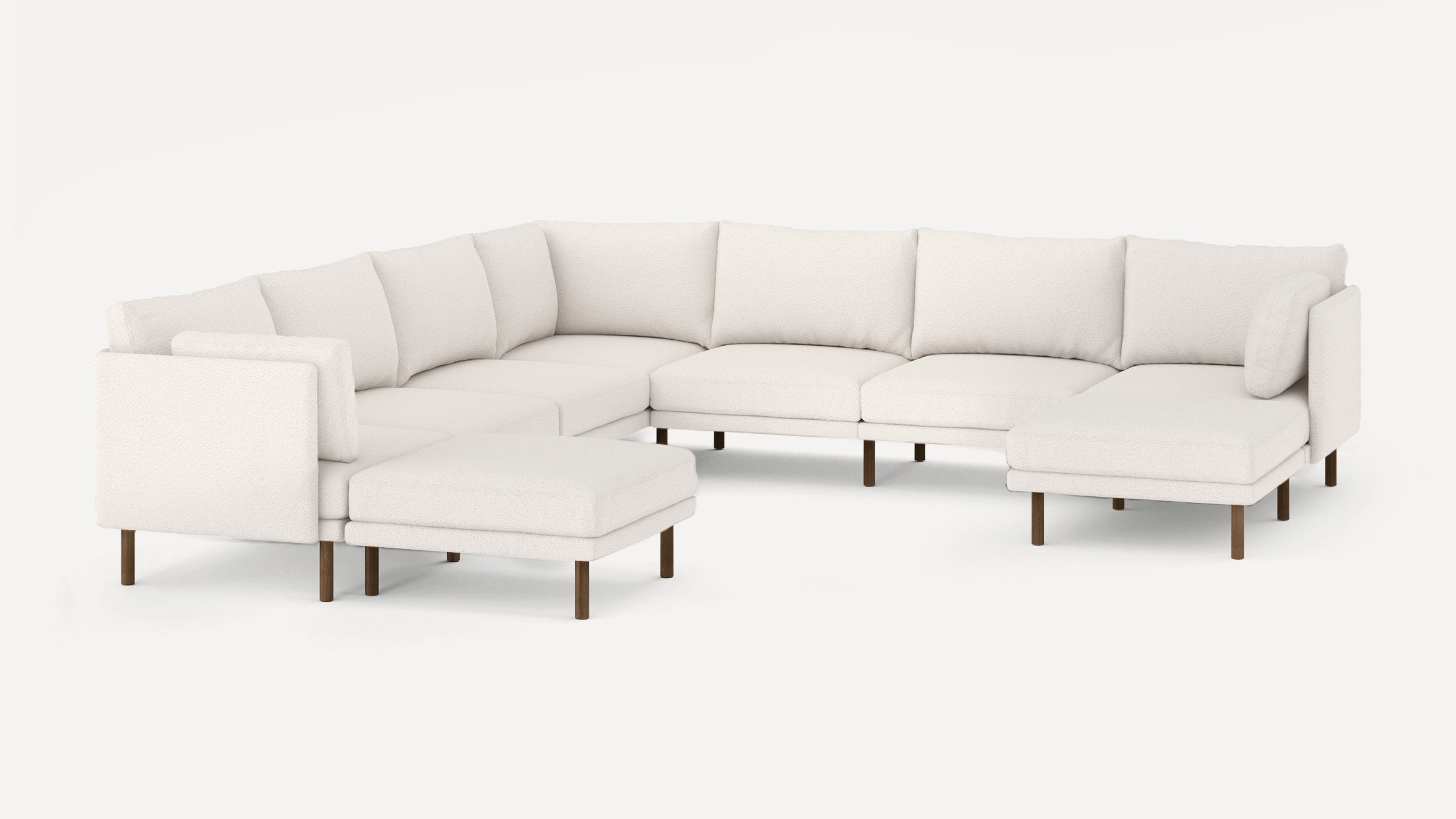 Large white L-shaped sectional sofa with low back cushions and wooden legs, featuring an ottoman and chaise lounge on each end.