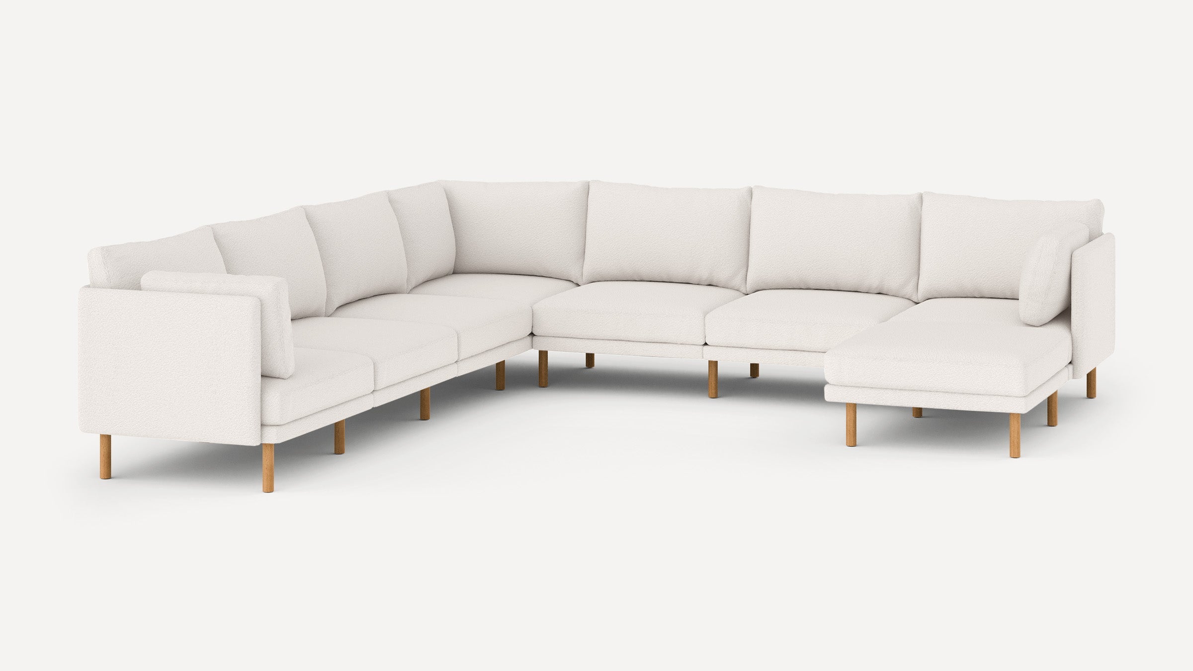 Modern L-shaped sectional sofa in white fabric with wooden legs and multiple back cushions, featuring a chaise lounge on one end.