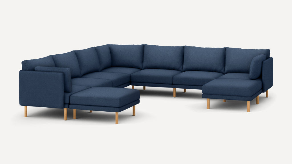 Large modern L-shaped sectional sofa in dark blue fabric with wooden legs and cushioned backrests.