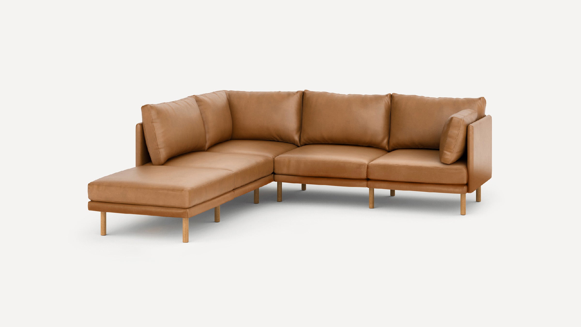Modern L-shaped sectional sofa in tan leather with wooden legs and plush back cushions on light background.