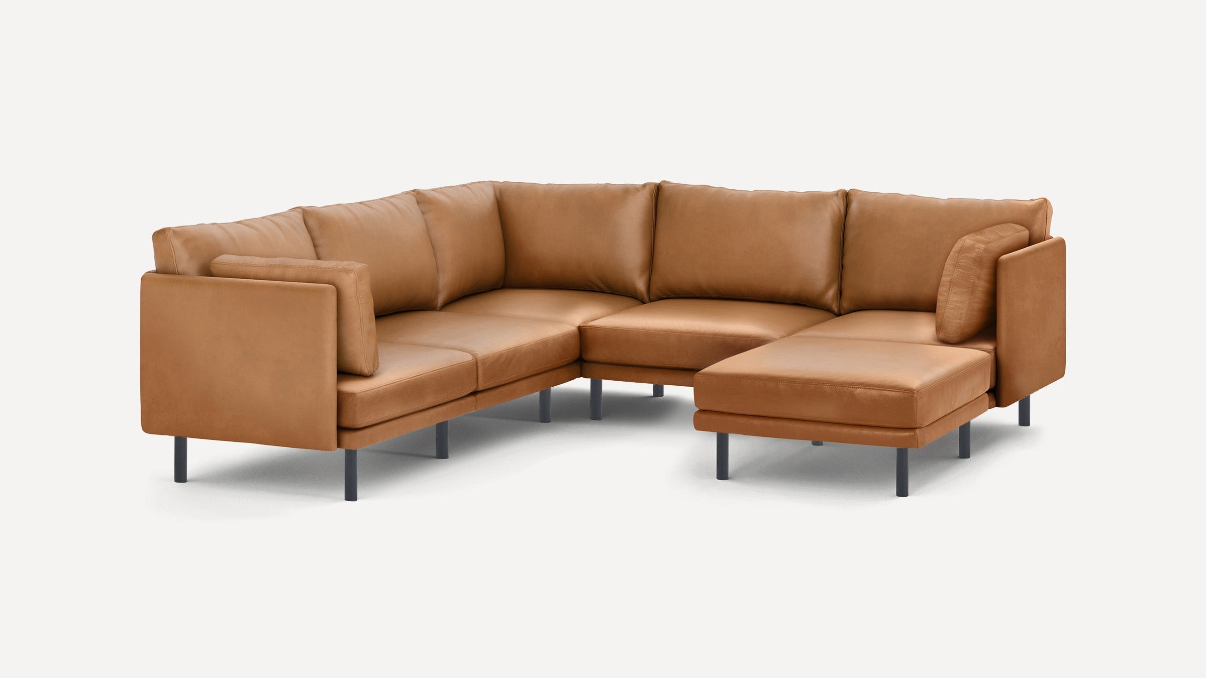 Modern L-shaped sectional sofa in tan leather with clean lines, cushioned backrests, and slim black legs.