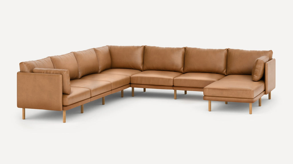 Large L-shaped sectional sofa in caramel brown leather with wooden legs and cushioned seats and backrests.