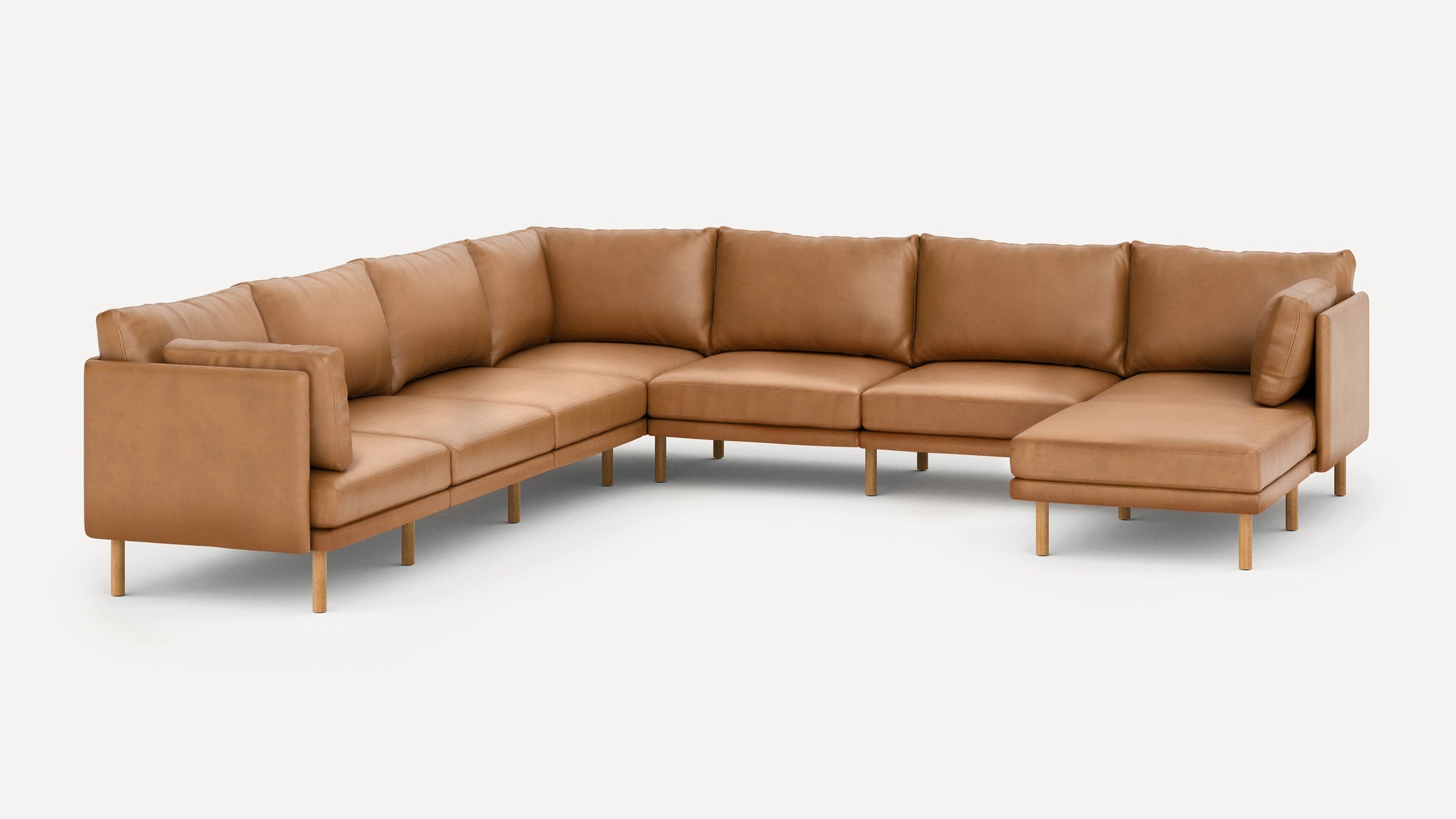 Large L-shaped sectional sofa in caramel brown leather with wooden legs and cushioned seats and backrests.
