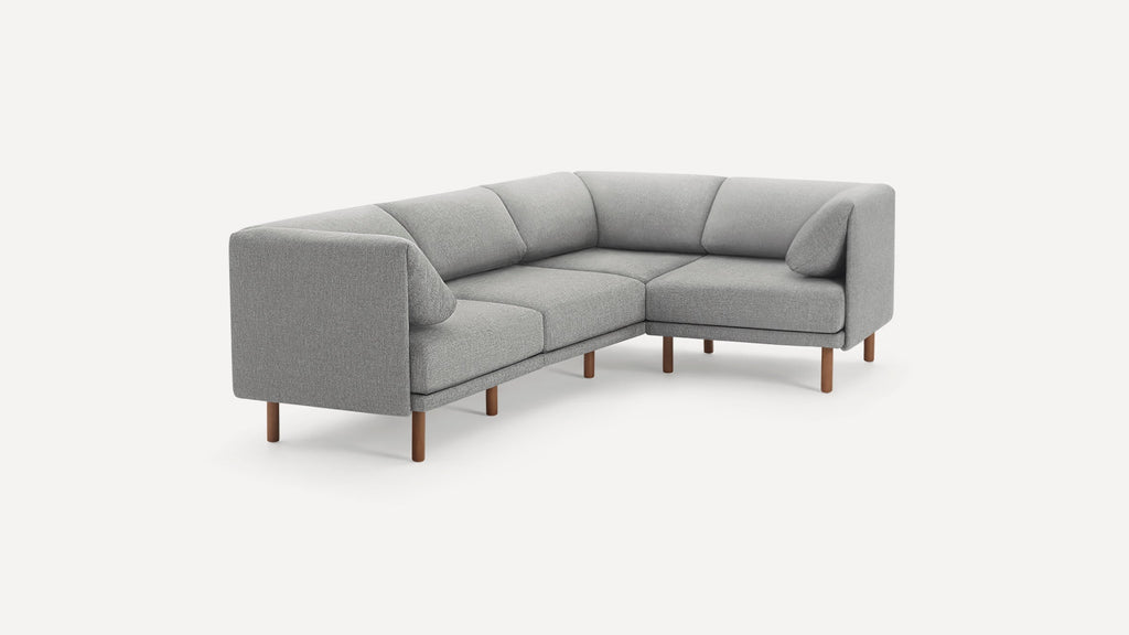Modern L-shaped grey fabric sofa with wooden legs, featuring cushioned seats and backrests, and two side pillows.