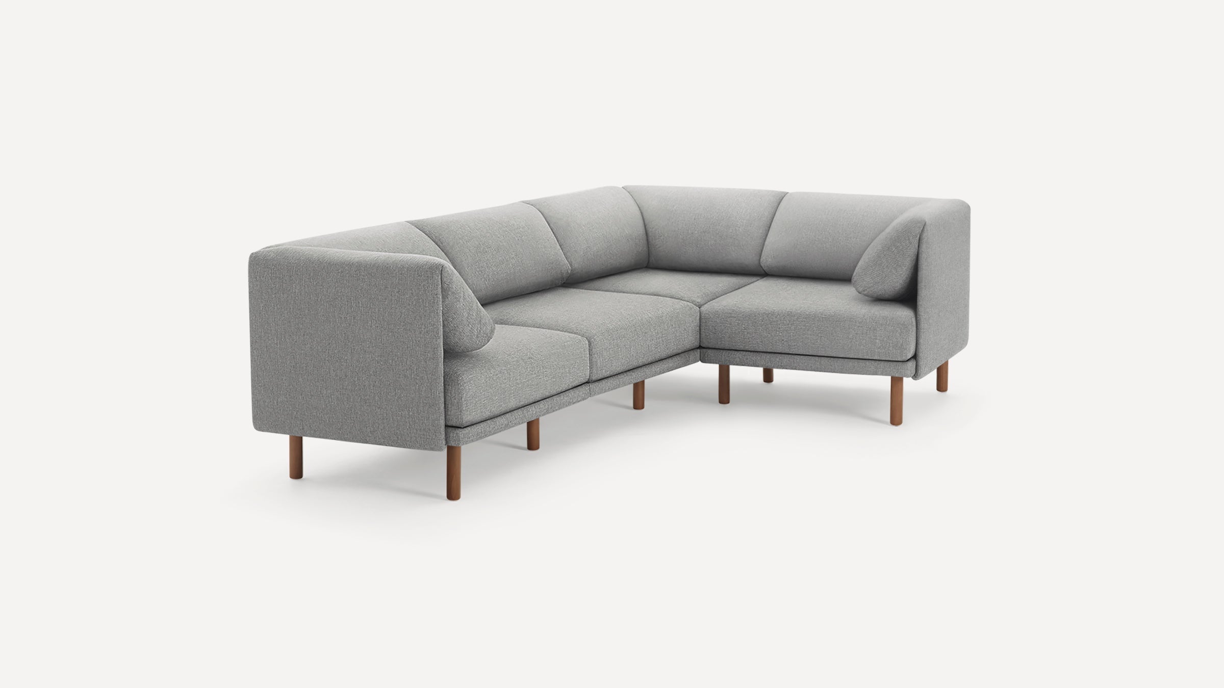 Modern L-shaped grey fabric sofa with wooden legs, featuring cushioned seats and backrests, and two side pillows.