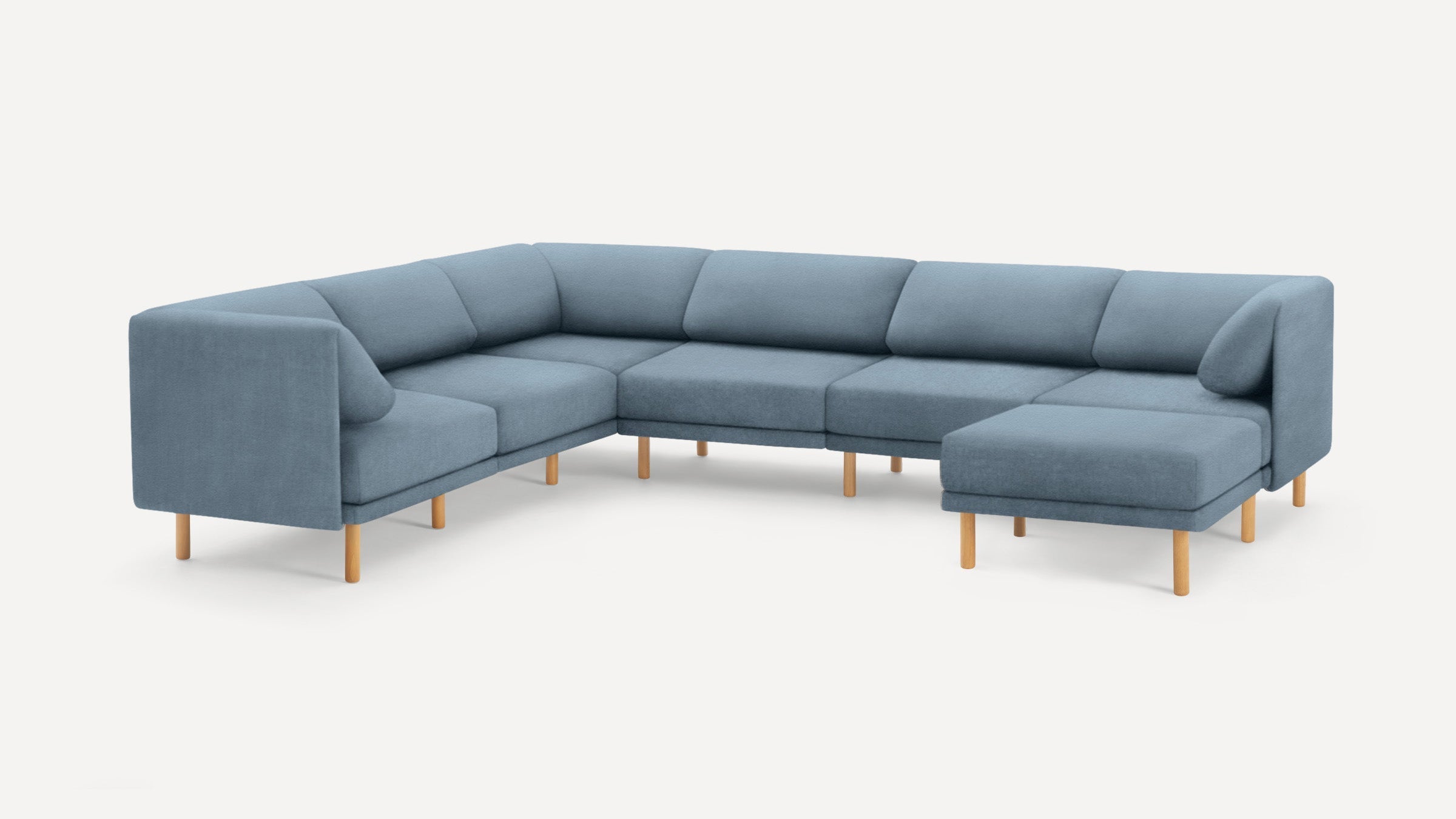 Large modern L-shaped sectional sofa upholstered in muted blue fabric with light wooden legs and cushioned backrests.