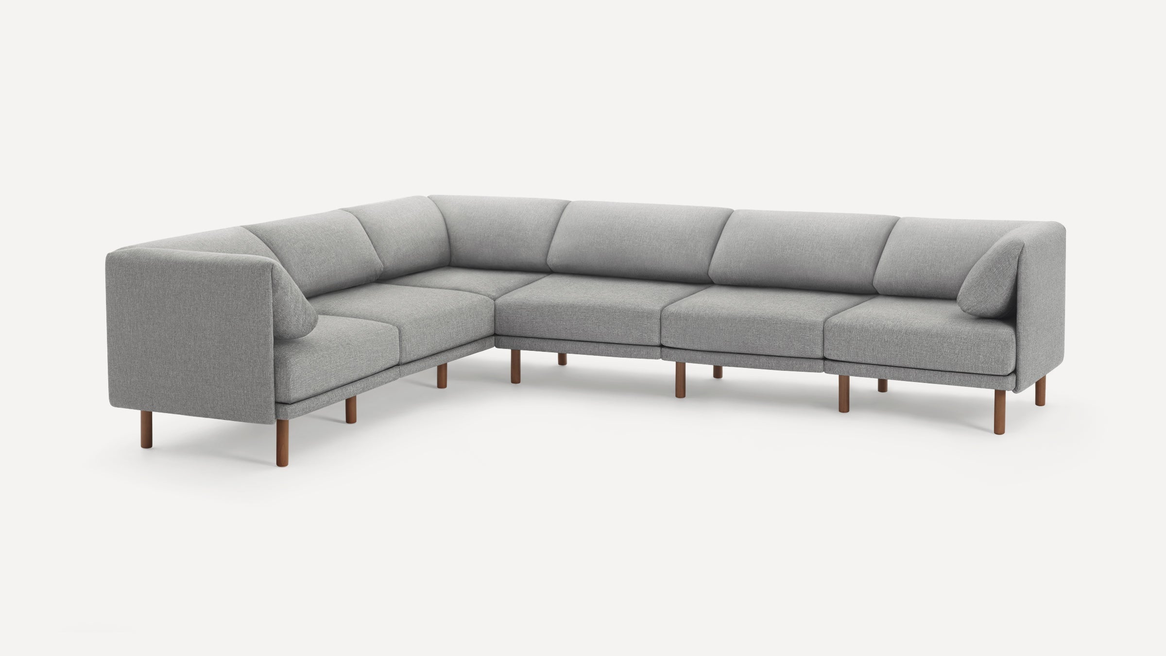 Modern L-shaped sectional sofa upholstered in light gray fabric with wooden legs and two small matching pillows.