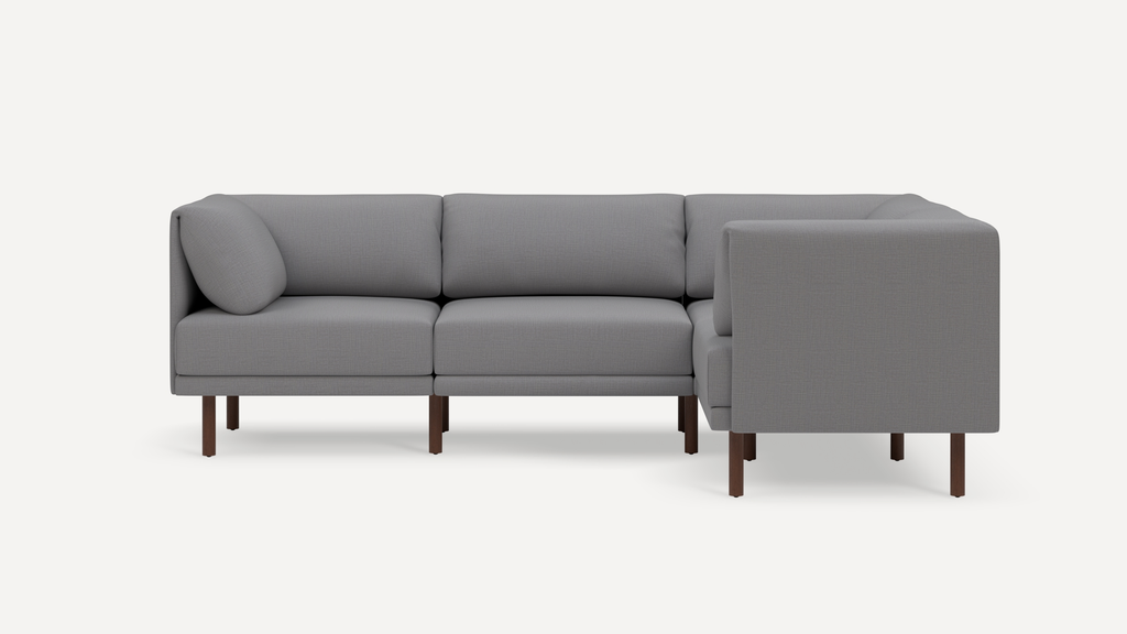 Modern gray L-shaped sectional sofa with wooden legs and plush back cushions, shown against a plain white background.