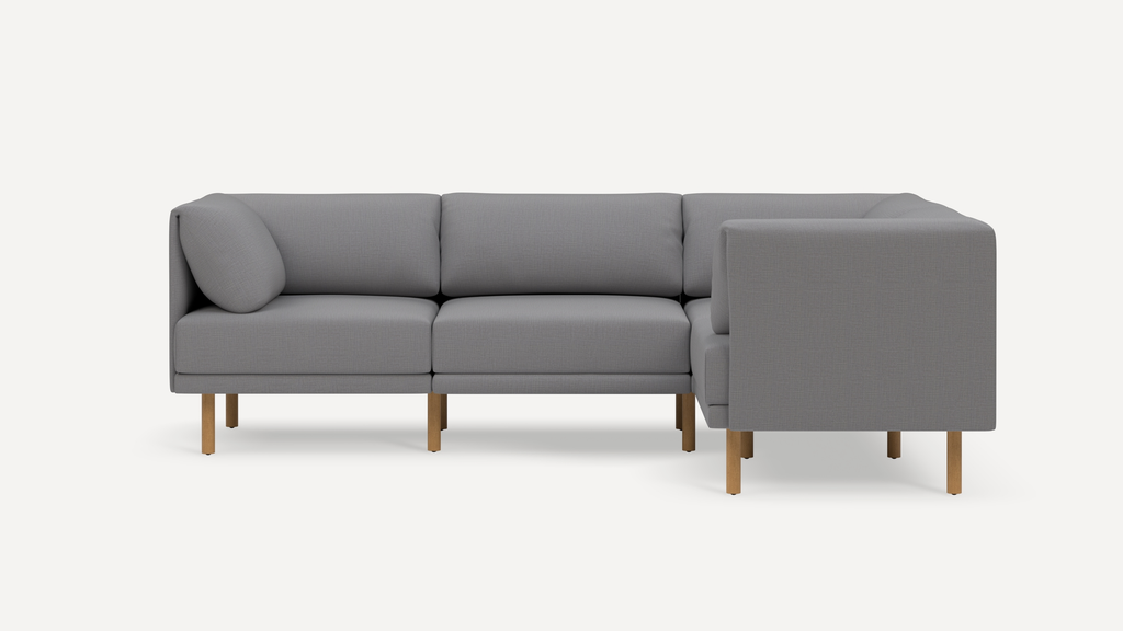 Modern L-shaped gray fabric sofa with wooden legs and cushioned backrests, displayed against a plain white background.