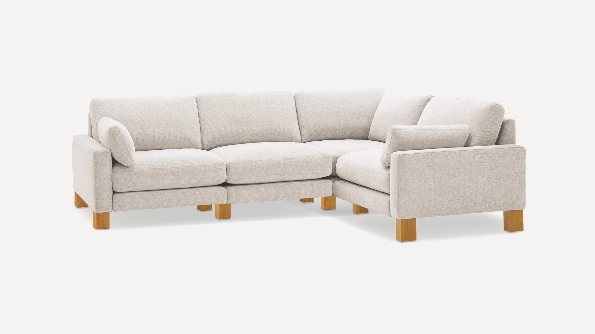 Light beige L-shaped sectional sofa with soft cushions and wooden block legs on a white background.