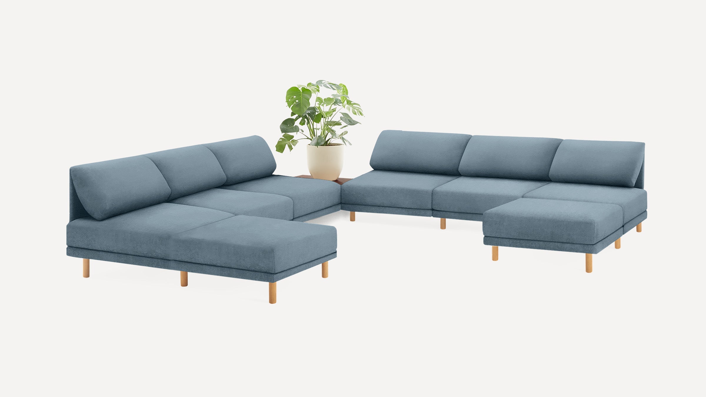 modern blue fabric sectional sofa with wooden legs and matching cushions, featuring a plant in a white background
