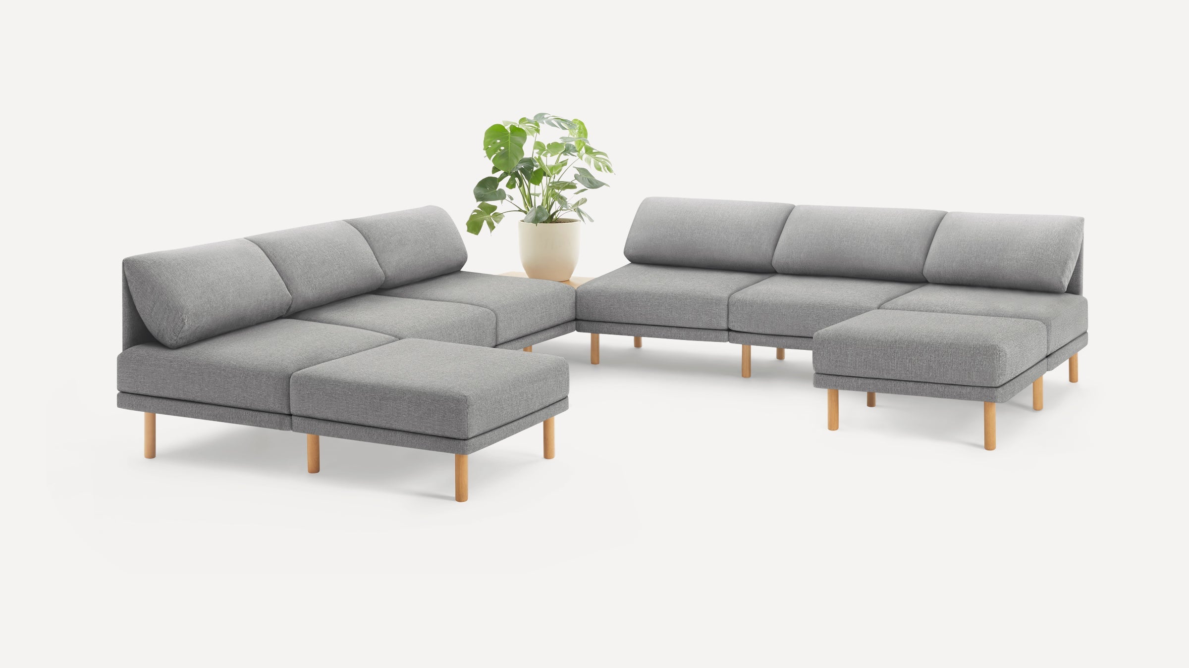 modern gray fabric sectional sofa with wooden legs and matching cushions, featuring a plant on the right side of the sectional sofa is on a white background