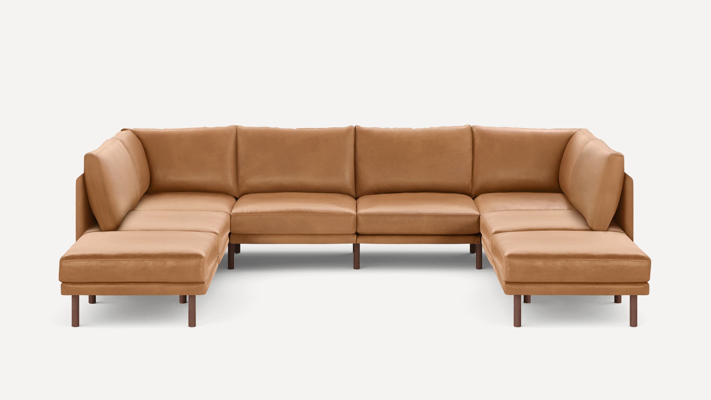 Large U-shaped sectional sofa in light brown leather with cushioned seats and backrests, supported by wooden legs.