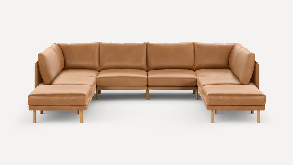 Large modern U-shaped sectional sofa with caramel leather upholstery and wooden legs on a plain white background.