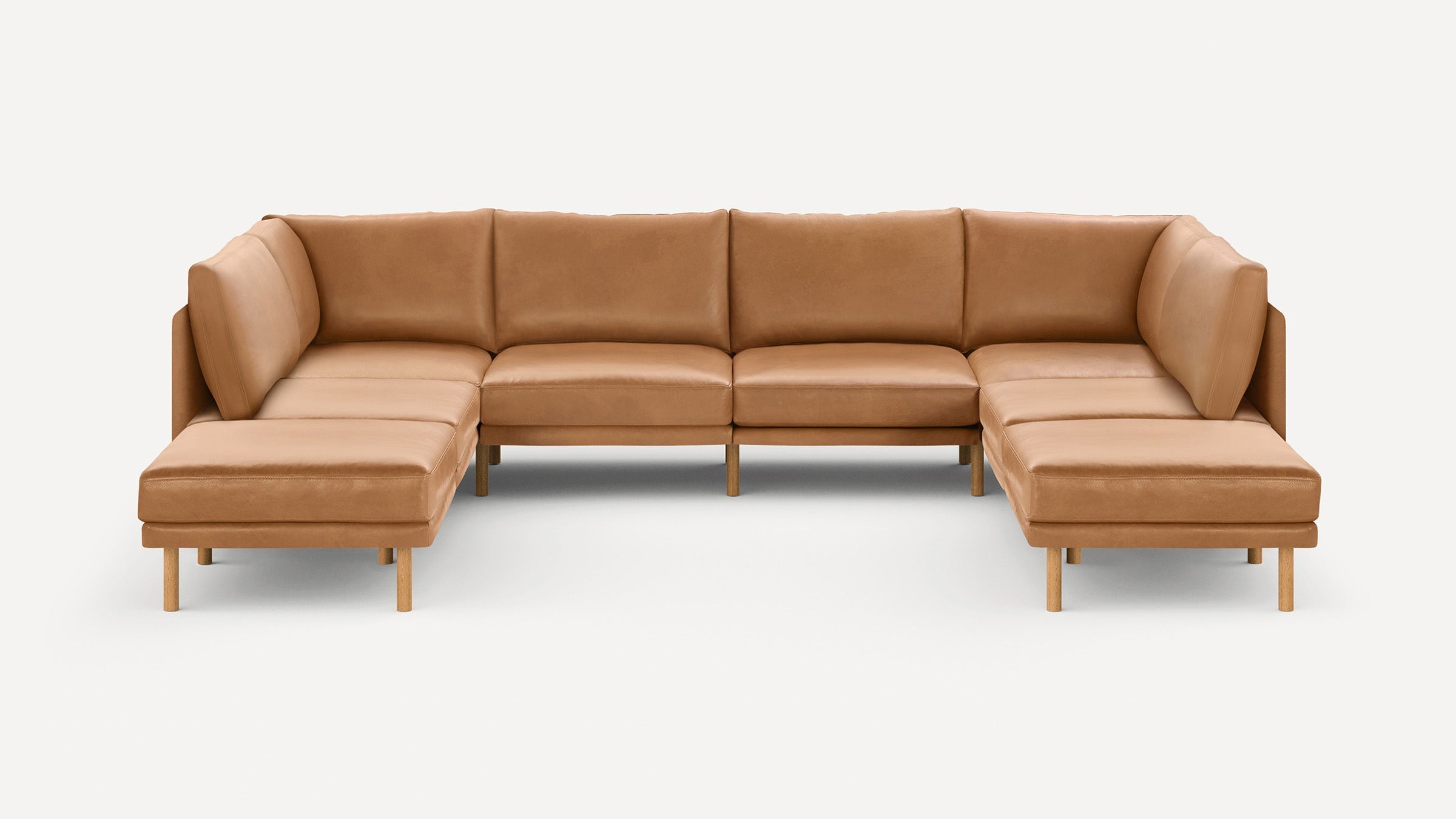 Large modern U-shaped sectional sofa with caramel leather upholstery and wooden legs on a plain white background.