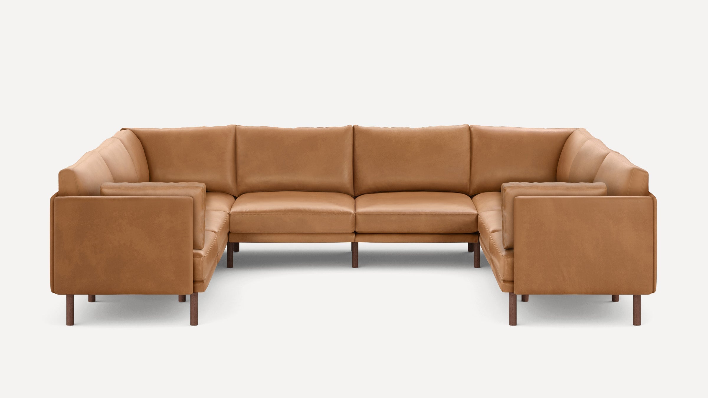 U-shaped sectional sofa in tan leather with padded armrests, back cushions, and dark wooden legs, set against a plain white background.