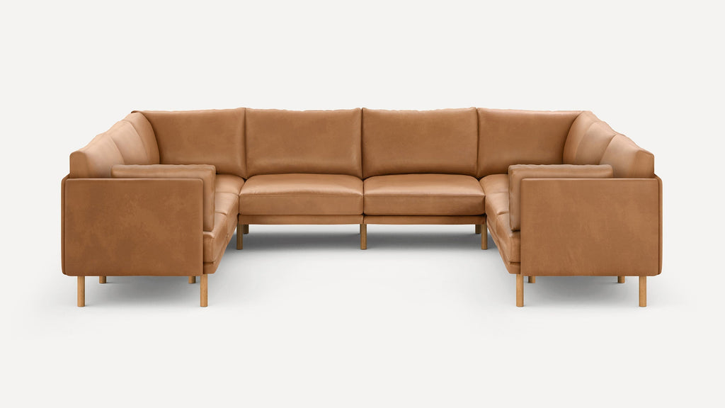 Large U-shaped sectional sofa with smooth tan leather upholstery and wooden legs, featuring cushioned back and armrests.