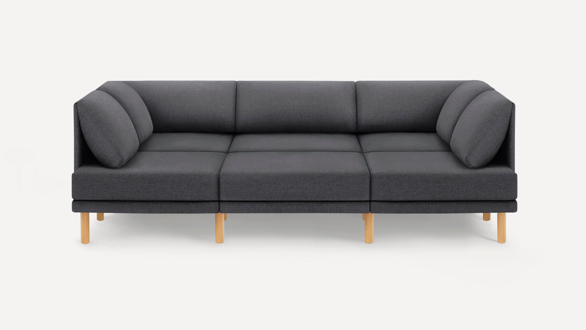 Modern dark gray fabric three-seater sofa with low backrest, cushioned armrests, and light wooden legs on a white background.