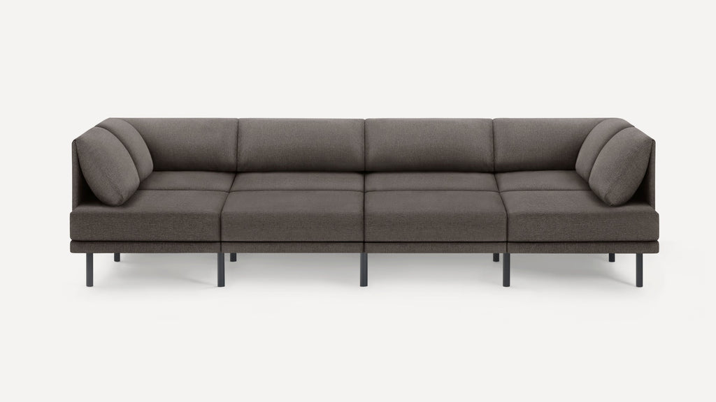 Modern, minimalist dark gray sectional sofa with four seat cushions and angled cushions on both ends, supported by slim black legs.