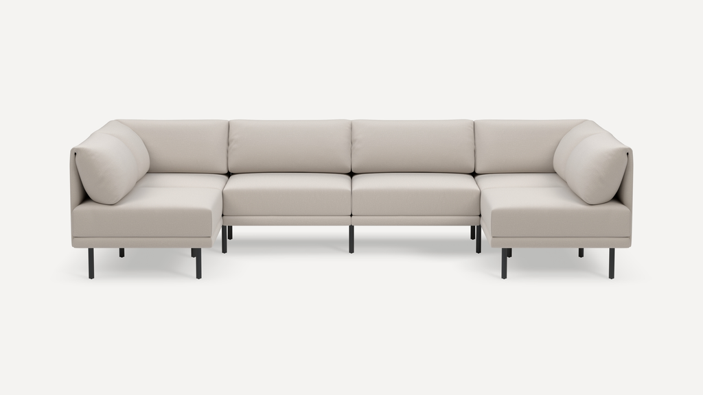 Modern beige sectional sofa with a minimalist design, elevated on slim black metal legs, featuring plush cushions and corner seating.