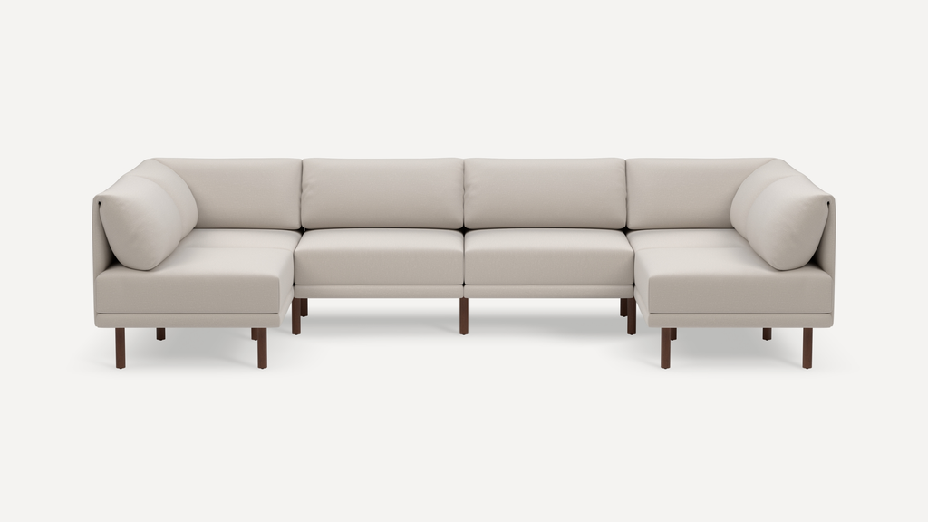 Large modern beige fabric sectional sofa with comfortable back cushions and dark wooden legs on a white background.