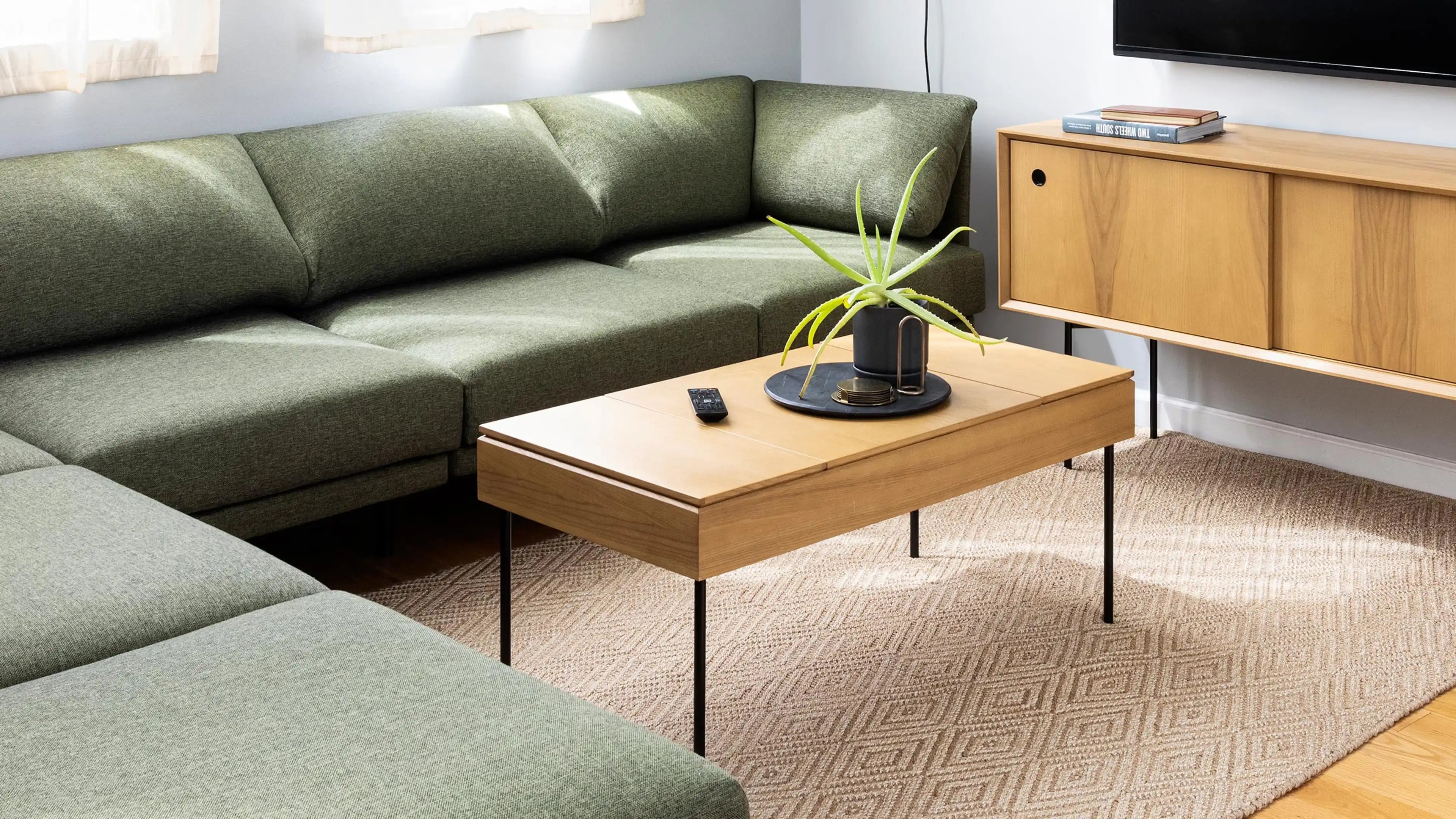 Modern living room with green sectional sofa, light wood coffee table with metal legs, decorative plant, and matching wooden TV console.