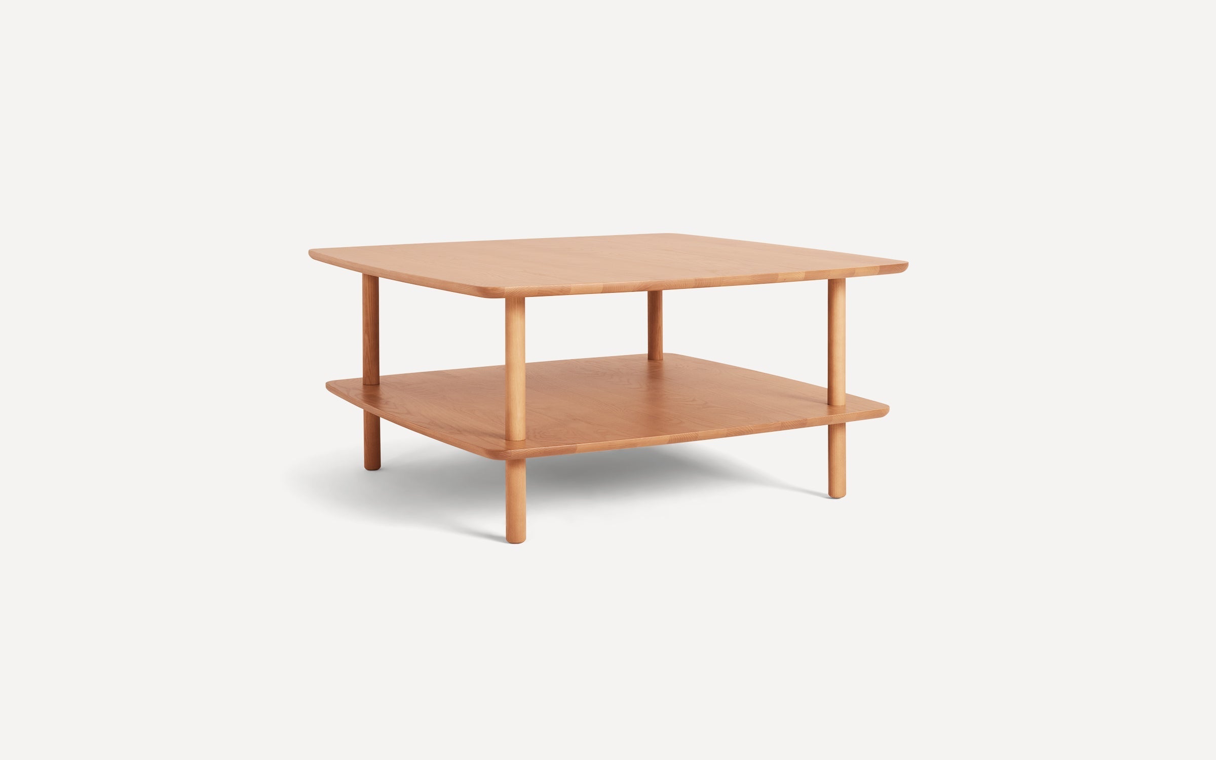Square wooden coffee table with rounded edges, two-tier design, and four cylindrical legs, light natural wood finish.