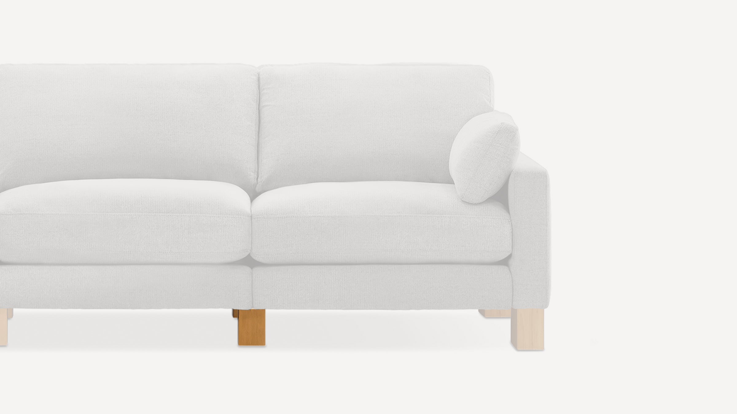 Partial view of a light gray fabric sofa with wooden legs and a matching round cushion on the right armrest.