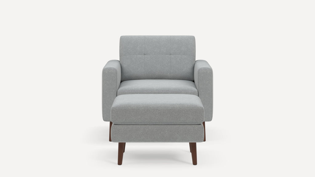 Front view of a modern light gray upholstered armchair with a matching ottoman and wooden legs on a white background.