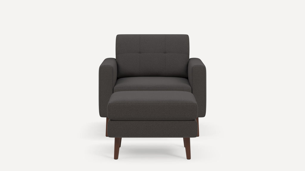 Dark gray upholstered armchair with matching ottoman, tufted backrest, and wooden tapered legs, shown against white background.