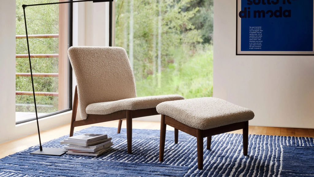 modern beige upholstered chair with matching ottoman and matching table with books on blue rug in living room
