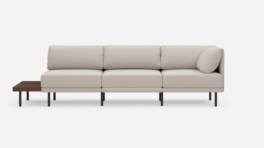 Modern beige fabric sectional sofa with three seat cushions, angled armrest, black metal legs, and attached dark wood side table.