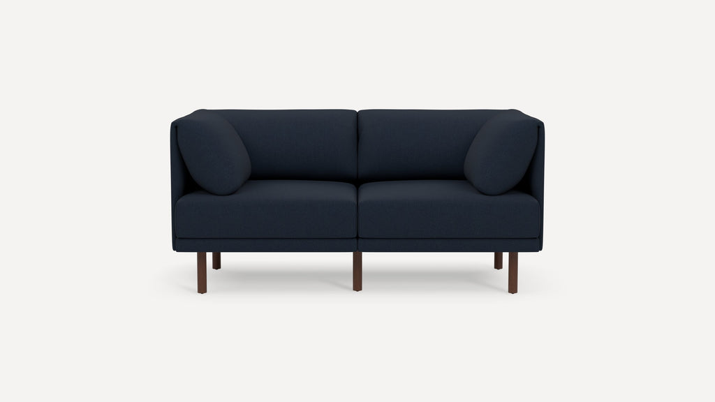 Modern navy blue two-seater sofa with rounded arm cushions and slim wooden legs on a white background.