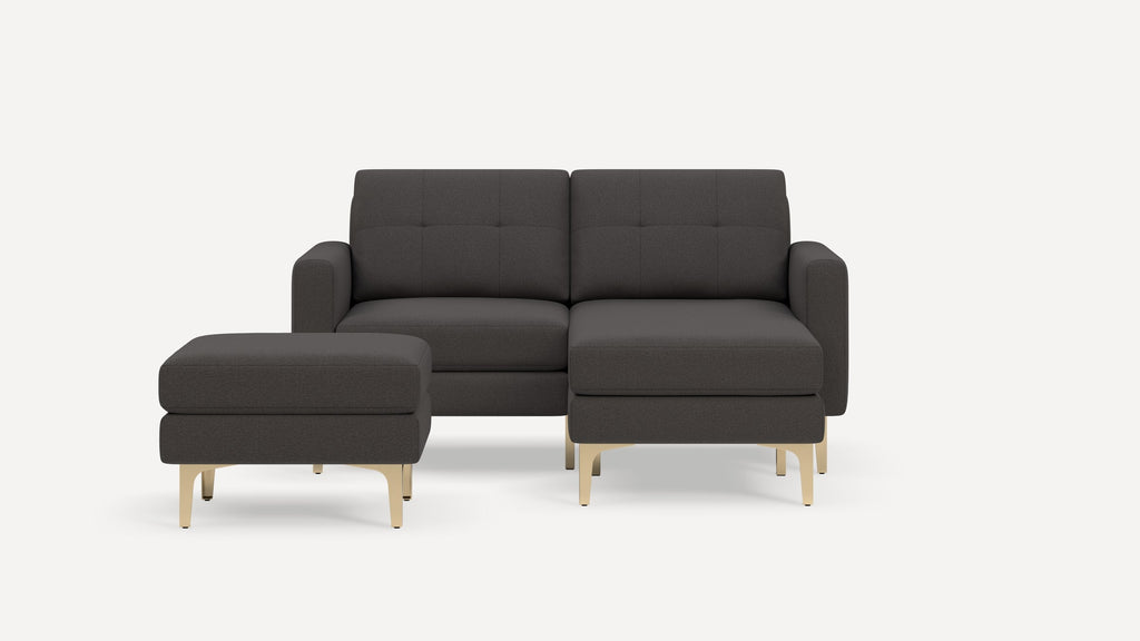 Dark gray fabric sectional sofa with tufted back cushions and matching ottoman, featuring gold-colored metal legs.