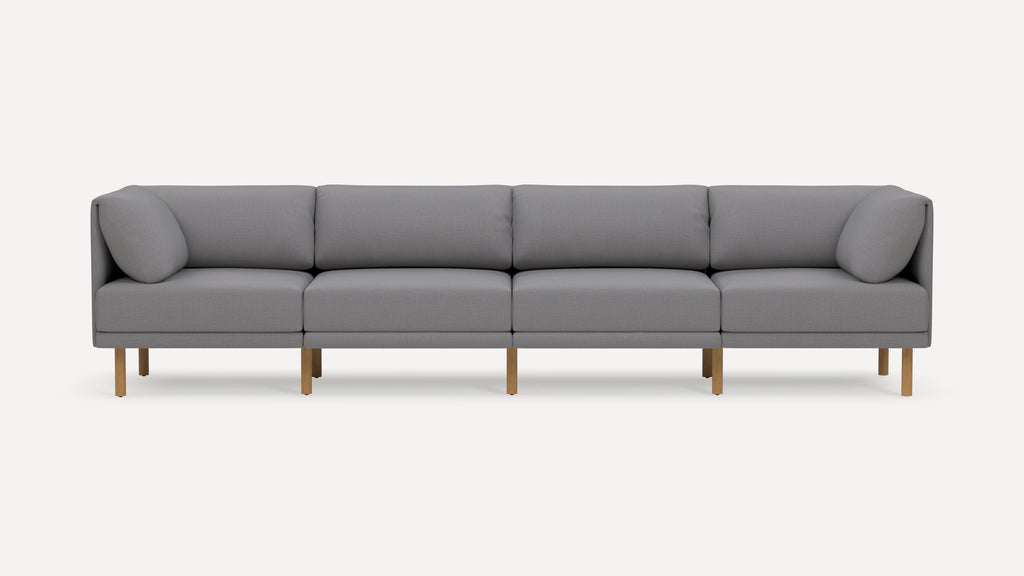 Modern light gray sectional sofa with wooden legs, featuring four seat cushions and two angled cushions on each end.