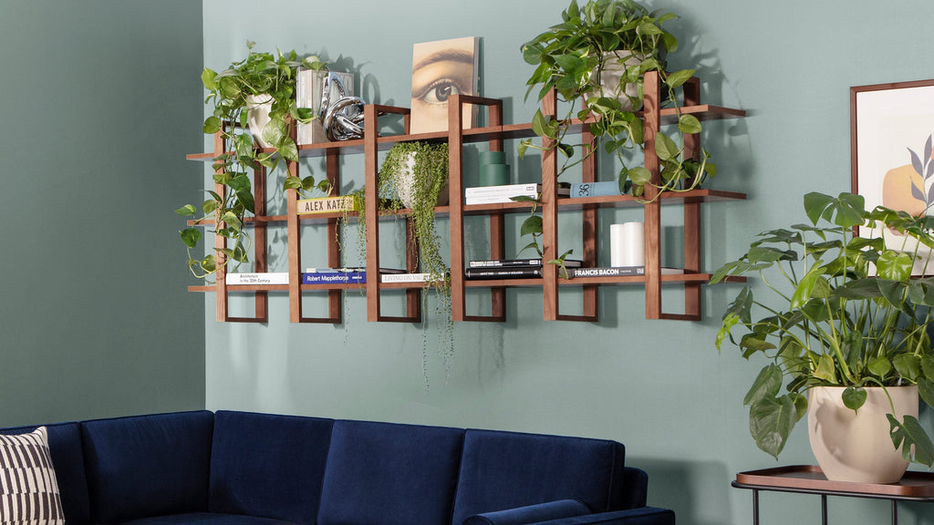 Wall-mounted wooden grid shelf with plants, books, and decorative items above a navy blue sofa in a contemporary living room.